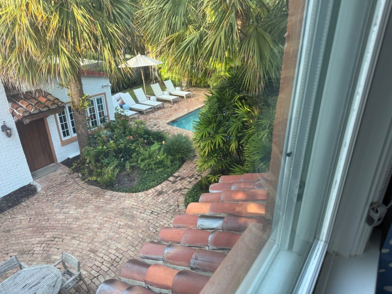 View from an upstairs window over the brick courtyard, palms, and pool loungers